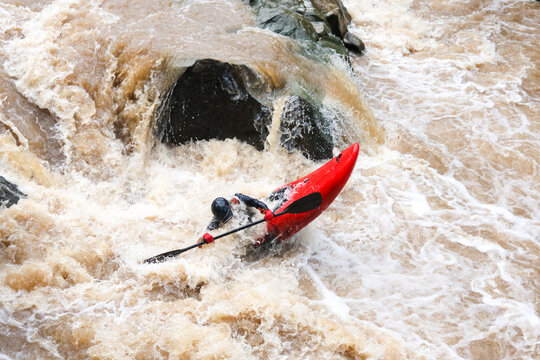 Whitewater kayaker battling turbulent river rapid and foamy waterfall near dark rock formation with intense outdoor adventure action and danger