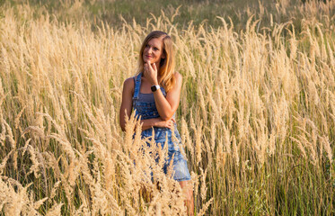 Obraz premium Pensive attractive woman posing in high dry grass field at sunset, beautiful rustic lifestyle portrait.