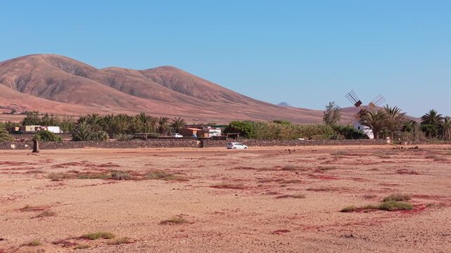 Aerial view of surroundings from El Cotillo, a coastal town located on the island of Fuerteventura, Canary Islands, Spain. Drone POV of windmill and car passing on the dirt road,