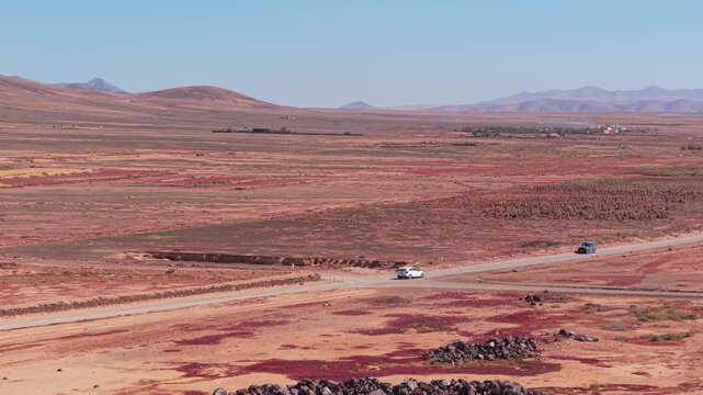 Aerial view of surroundings from El Cotillo, a coastal town located on the island of Fuerteventura, Canary Islands, Spain. Drone POV od the mountains and car passing on the dirt road.