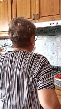 Joyful senior woman with glasses playfully dancing and having fun while cooking in her home kitchen, expressing happiness and enjoying her retirement with lighthearted movements