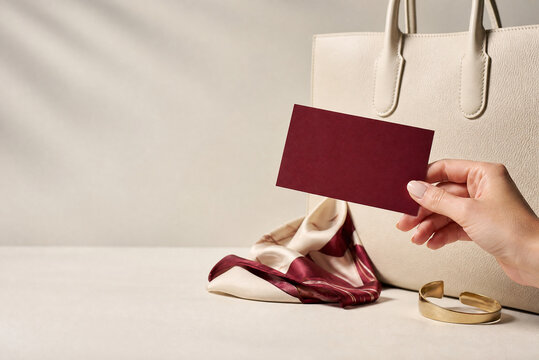 Minimalist business card mockup held by hand, elegant burgundy card with leather tote bag, luxury fashion accessories and stationery