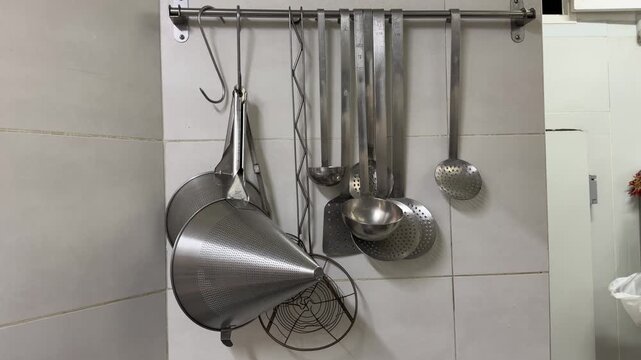 Stainless steel kitchen utensils hanging on a tiled wall