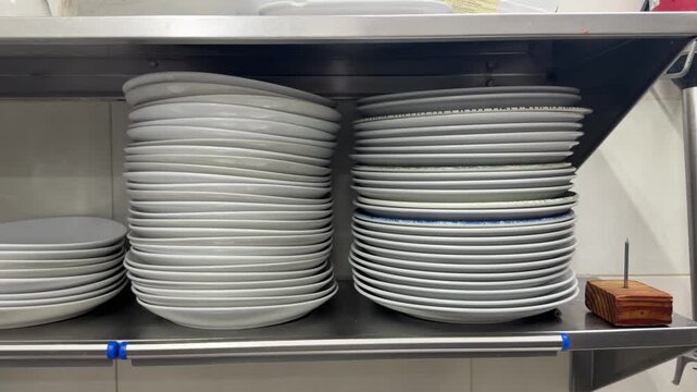 Clean white plates stacking on restaurant kitchen shelves