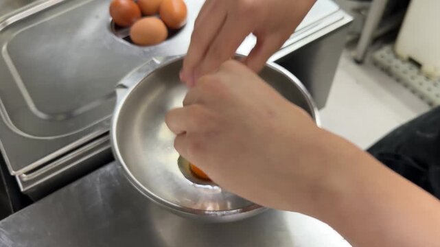 Chef cracking fresh brown eggs into a stainless steel bowl