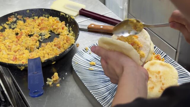 Chef stuffing arepas with scrambled eggs in a kitchen