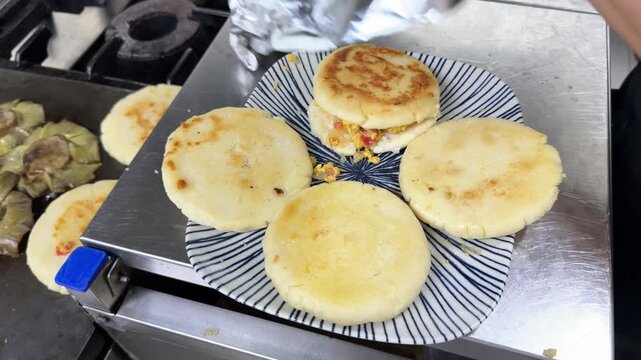Chef cooking traditional arepas on a grill in a restaurant kitchen