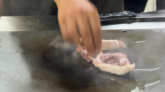 Chef cooking lamb chops on a hot griddle in a restaurant kitchen