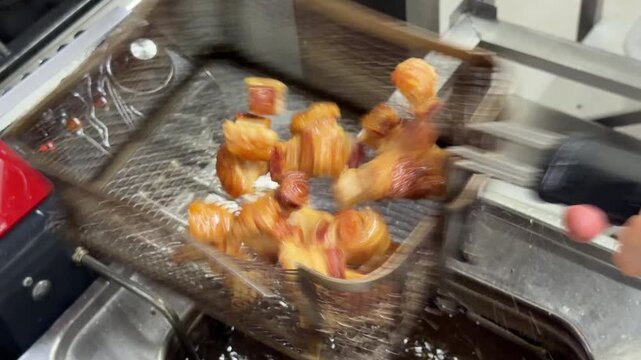 Chef deep frying bacon wrapped appetizers in a commercial kitchen fryer