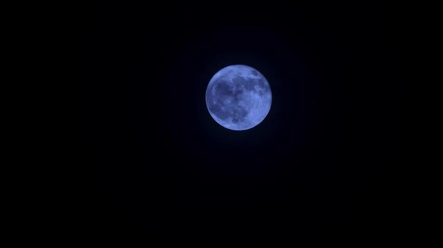 Blue moon conceptual video featuring a sharp full moon with thin clouds passing by in real time