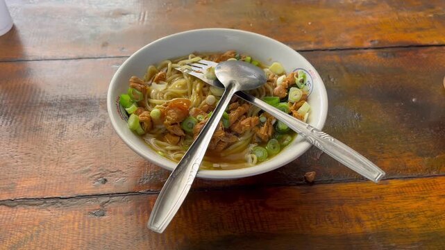 Authentic Indonesian mie ayam or chicken noodles served with spoon and fork in a bowl on a rustic wooden table
