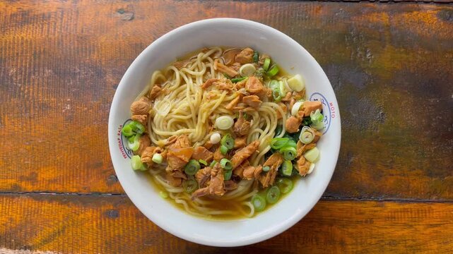 High angle shot of authentic Indonesian mie ayam or chicken noodles with rich savory sauce in a ceramic bowl