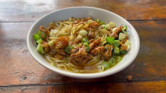 Close up shot of authentic Indonesian mie ayam or chicken noodles served hot in a bowl on a rustic wooden table