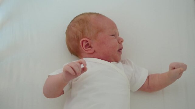 Newborn lies in crib and moves arms chaotically, showing restless activity, immature coordination, and active wakefulness during uneasy moment of early infancy in safe home setting indoors.