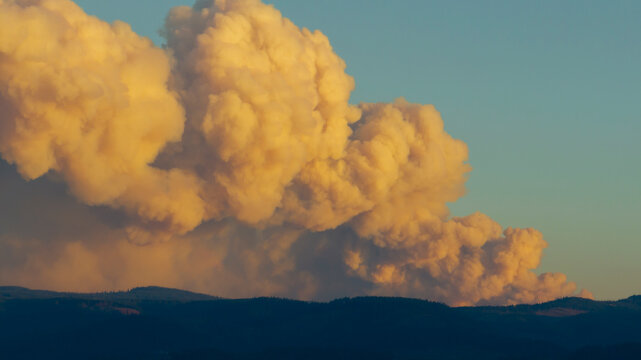 Wildfire smoke billows over mountains at sunset