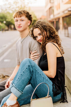 Stylish young couple sitting together on a curb