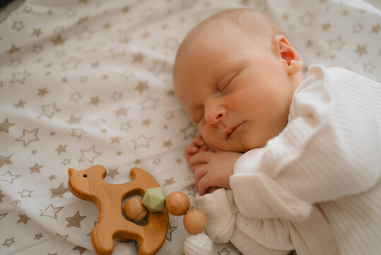 Newborn baby sleeps deeply on a star patterned sheet next to a natural wooden bear toy, representing the delicate stage of infant development, early childhood, and the innocence of new beginnings