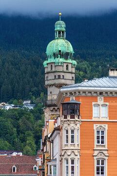 Torre Civica (Stadtturm) e palazzo arancione a Innsbruck con montagna boscosa sullo sfondo, Tirolo, Austria
