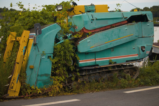 Abandoned Teal and Yellow Industrial Machine Overgrown with Green Vines by an Asphalt Road