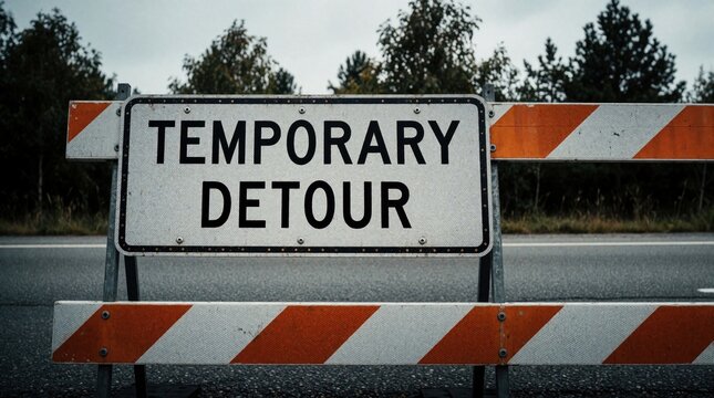 Roadside temporary detour sign on barricade. Barrier blocks traffic, reroutes cars and trucks. Construction or road work may cause delay, need for alternate route.