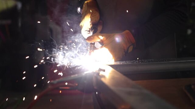 Arc welding metalworking worker creates bright welds and flying sparks steel beam dark workshop, wearing protective glove during careful industrial fabrication, cutting and joining metal with focused