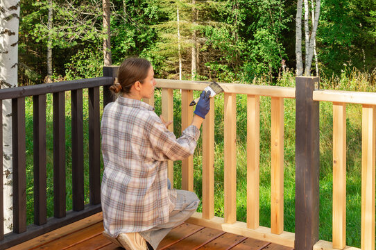 Woman applying graphite wood oil to a wooden terrace railing with a brush. DIY home improvement, deck maintenance and wood treatment.