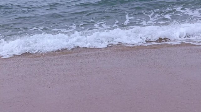 Gentle ocean waves rolling onto a sandy beach and foaming in slow motion