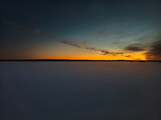 Obraz premium Minimalist long shot of a vast snow-covered frozen lake under an orange sunrise horizon in Lapland, Finland