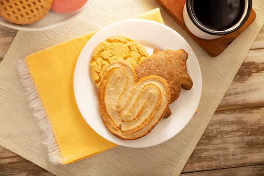 Traditional Mexican sweet bread variety on a rustic wooden board. Variety of authentic pan dulce including puerquito, orejas, and cookies over a neutral tablecloth background for bakery concept.
