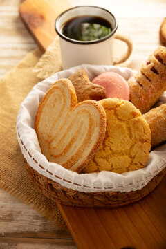 Traditional Mexican sweet bread variety on a rustic wooden board. Variety of authentic pan dulce including puerquito, orejas, and cookies over a neutral tablecloth background for bakery concept.