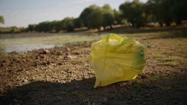 Yellow plastic waste bag left on a river shoreline. Concept of environmental plastic pollution, aquatic contamination, conservation efforts, and plastic waste management. 4K.