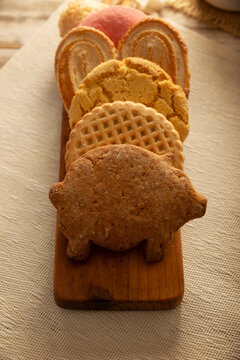 Traditional Mexican sweet bread variety on a rustic wooden board. Variety of authentic pan dulce including puerquito, orejas, and cookies over a neutral tablecloth background for bakery concept.