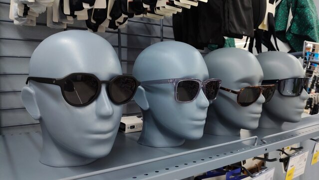 Sunglasses displayed on mannequin heads on a shelf in a retail store. Row of plastic mannequin heads wearing various sunglasses models in a shop.
