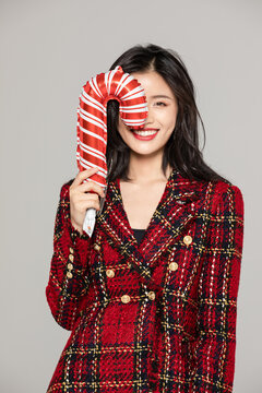 Smiling young woman with oversized candy cane in festive red outfit