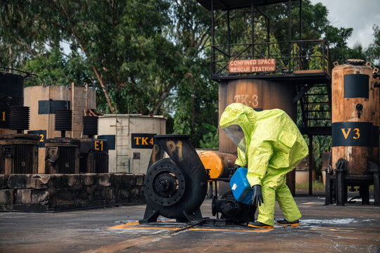 Hazmat worker handling chemical spill cleanup beside industrial pump equipment during emergency response training at a factory site while wearing full protective suit and respirator