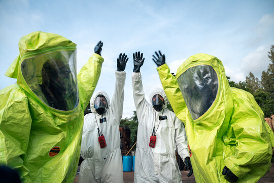 Hazmat response team raising gloved hands after completing emergency preparedness training and a workplace safety exercise at an industrial facility in full protective suits