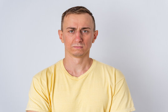 Middle aged man in a yellow t shirt, short hair, looking straight at the camera with a serious, displeased expression conveying concern, disappointment and frustration on grey background