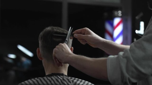 Skilled barber trimming client's hair with precision scissors, working inside vintage styled barbershop featuring traditional red white blue pole