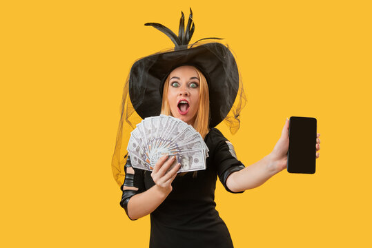 Excited woman dressed as a witch holding a fan of cash and a blank smartphone, representing online earnings, financial surprise, or digital Halloween promotions
