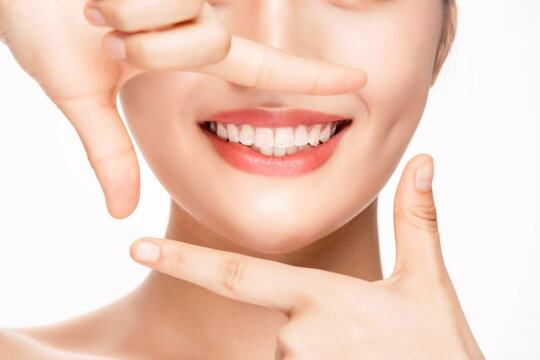 Smiling woman framing mouth with fingers showing white teeth
