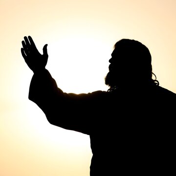 Silhouette of a person raising their hand towards light