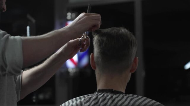 Skilled barber trimming client's hair with precision scissors, working inside vintage styled barbershop featuring traditional red white blue pole