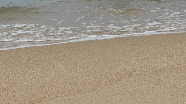 Gentle ocean waves washing over a sandy shoreline, showing clear sea water and coastal sediments of Aqua Marina