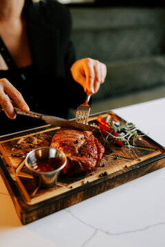 Person cutting a cooked beef steak with metal cutlery on a wooden board during dinner in a cafe
