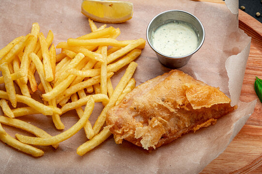 Fish and fries with sauce and lemon. A meal consisting of fried fish, golden fries, and a small cup of sauce with a slice of lemon on the side.