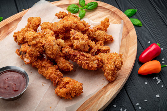 Breaded chicken strips on wooden tray. Golden deep fried chicken tenders served with sauce and green basil on parchment paper.