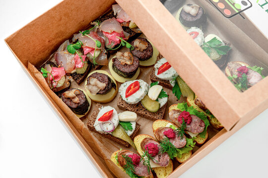 Assorted food items in a takeout box. Different types of food are arranged in a takeout box. There are bread slices topped with various ingredients.