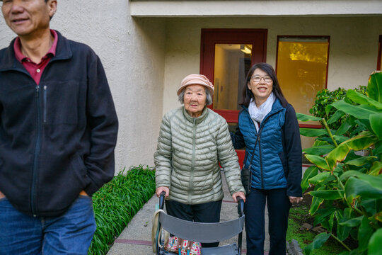 Family outing. Senior woman walking using a mobility walker, accompanied by her adult daughter and son. California.
