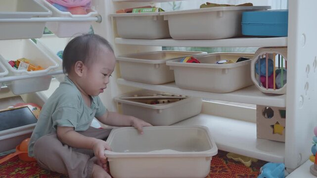 A young child is engaged in organizing toys in a playroom, focusing on tidiness and play. The scene captures curiosity and the joy of play in a nurturing environment.