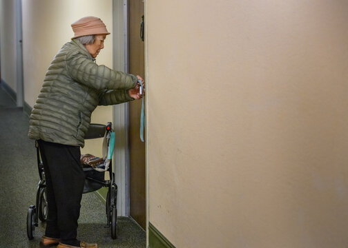 Elderly woman locks the apartment door using a key, mobility walker by her side. Independent living concept. California.